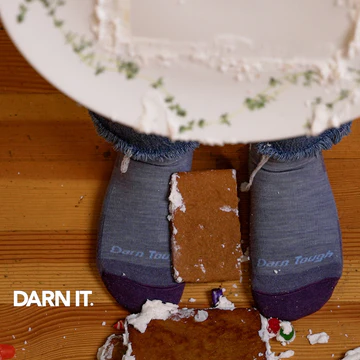 Darn It - feet wearing Darn Tough socks next to a destroyed gingerbread house